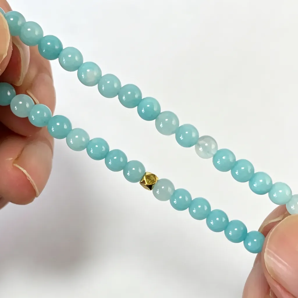 Aquamarine bracelet held in hand, stretched open to show the full strand of translucent blue beads and the elastic cord